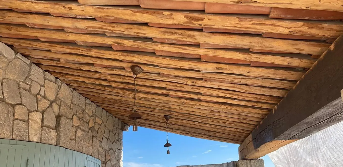 Plafond en bois et poutres apparentes aérogommés sous un auvent en pierre